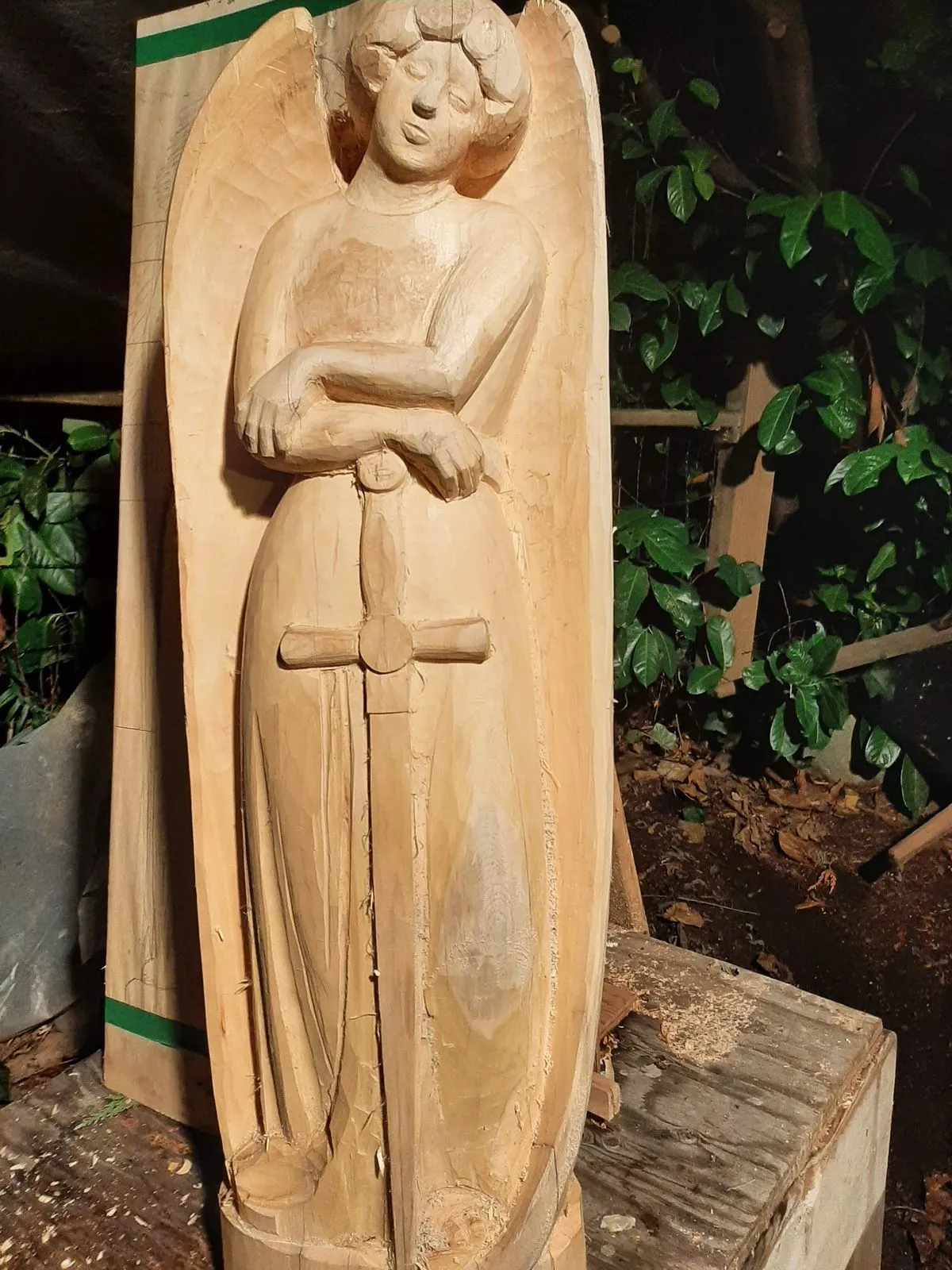 A life-size robed figure being carved from a solid timber baulk