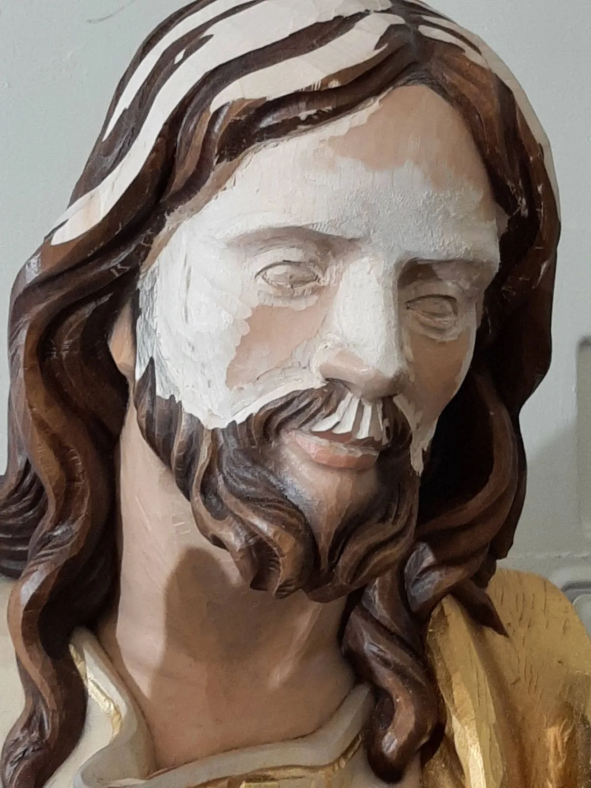 A carved statue with the face stripped back to bare primer during restoration