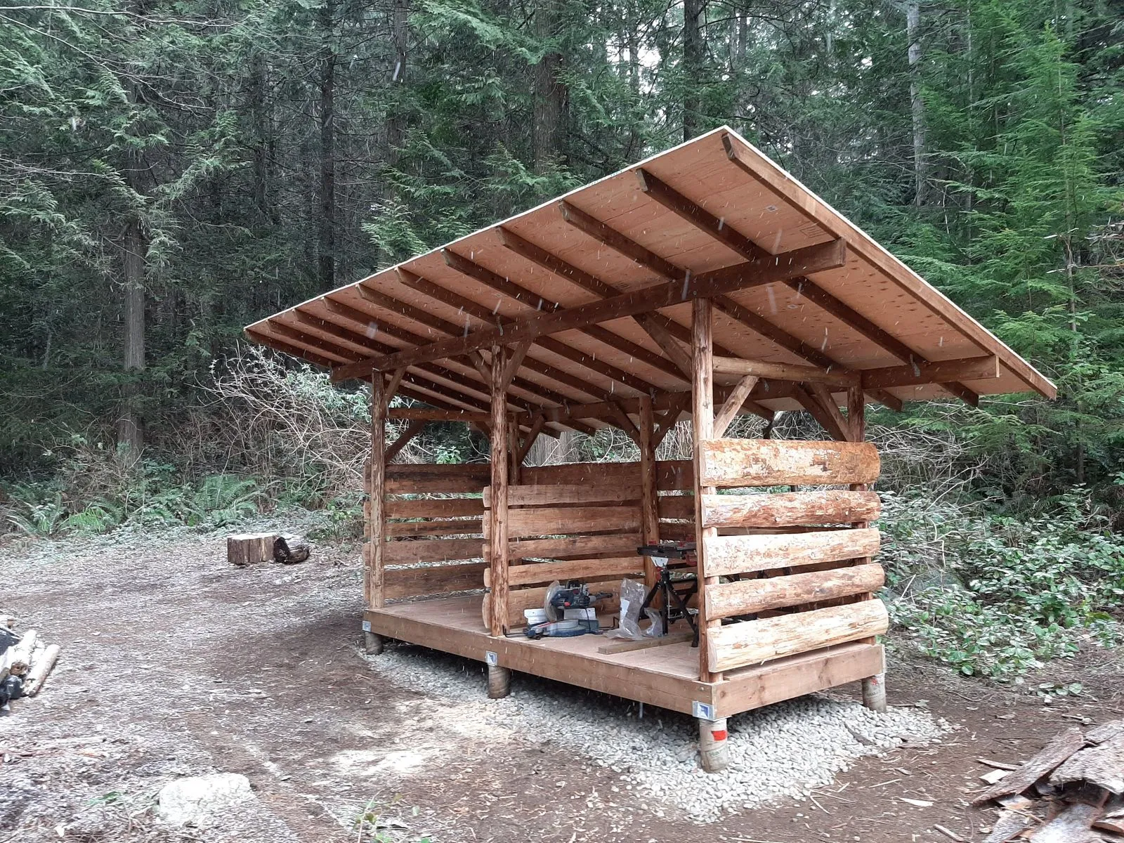 A timber-framed woodshed on log posts